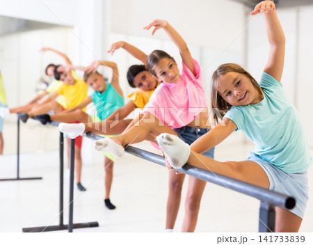 Cheerful girl working near ballet barre during group choreography class Cheerful girl working near ballet barre during group choreography class 141733839
