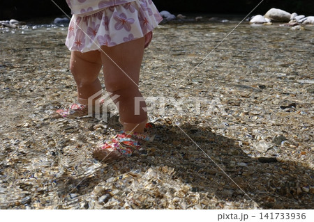 透明な川でサンダルを履いて入る1歳の子どもの足元。清流の浅瀬 141733936