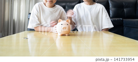 Two sister kids build healthy money habits through playful saving future planning, wealth growth and financial literacy in front of black leather sofa at home. Two sister kids build healthy money habits through playful saving future planning, wealth growth and financial literacy in front of black leather sofa at home. 141733954