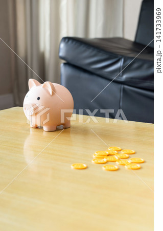 Piggy bank, and a little coin show a simple personal finance on old small table surface with black sofa background. Piggy bank, and a little coin show a simple personal finance on old small table surface with black sofa background. 141733969