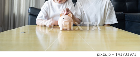 Kids happily deposit coins into a piggy bank, representing childhood savings, teamwork, and early financial responsibility. Kids happily deposit coins into a piggy bank, representing childhood savings, teamwork, and early financial responsibility. 141733973