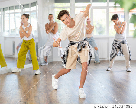 Teen guy together with group of teenage friends, learn to dance hip hop in choreographic hall. Teen guy together with group of teenage friends, learn to dance hip hop in choreographic hall. 141734080