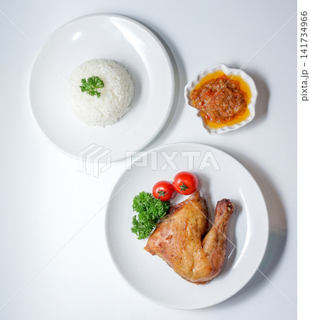 Overhead view of a chicken rice meal featuring roasted chicken leg, steamed white rice, chili sauce, and garnish. Suitable for Asian food concepts, restaurant menus, and editorial use. Overhead view of a chicken rice meal featuring roasted chicken leg, steamed white rice, chili sauce, and garnish. Suitable for Asian food concepts, restaurant menus, and editorial use. 141734966