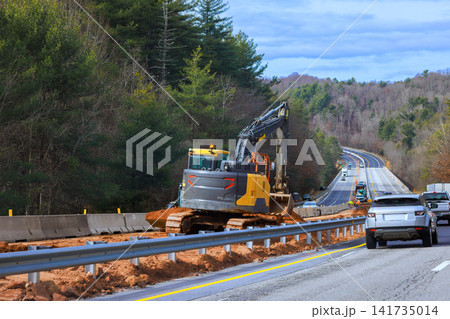 Heavy machinery is working on side of highway as cars drive by Heavy machinery is working on side of highway as cars drive by 141735014