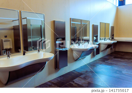 Restroom with several sinks, mirrors bright lights highlight clean design in public area. 141735017