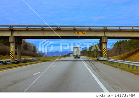 Truck drives on highway under large bridge with hills on North Carolina Truck drives on highway under large bridge with hills on North Carolina 141735484