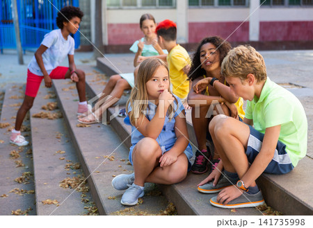 Positive tweenagers friendly blabbing while sitting on steps outdoors 141735998