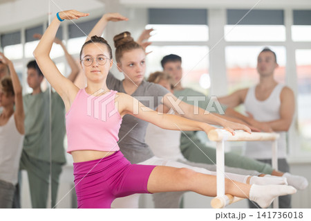 Teen ballet students prepare for classes, near ballet bare stretch legs under man teacher guidance Teen ballet students prepare for classes, near ballet bare stretch legs under man teacher guidance 141736018