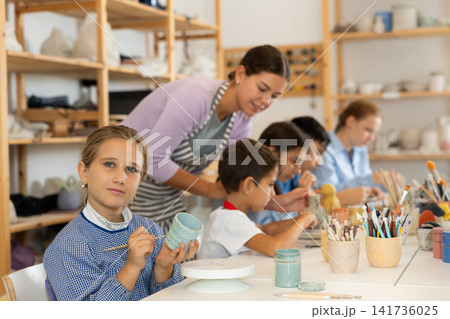 Little girl painting handmade ceramic cup with brush 141736025
