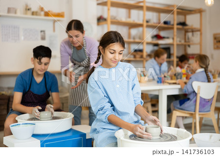 Children working at potter's wheel with teacher in art studio 141736103