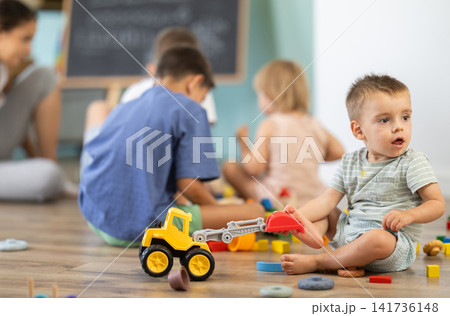 Baby boy playing with wooden toys on floor in kindergarten Baby boy playing with wooden toys on floor in kindergarten 141736148