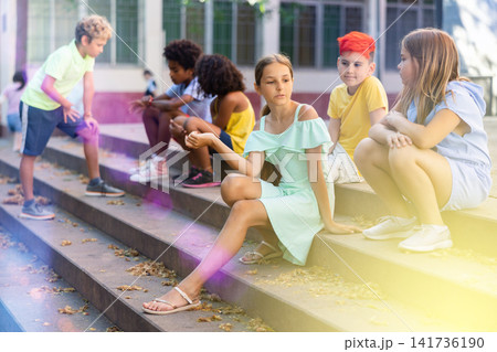 Children talking together while sitting on stairs outdoors Children talking together while sitting on stairs outdoors 141736190
