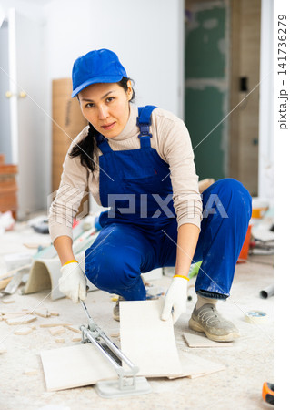 Woman builder cuts ceramic tiles with tile cutter Woman builder cuts ceramic tiles with tile cutter 141736279