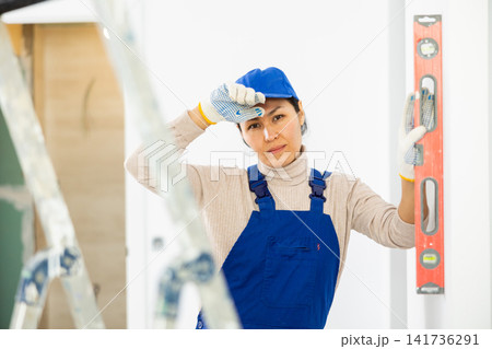 Woman builder using building level measures the vertical of wall Woman builder using building level measures the vertical of wall 141736291