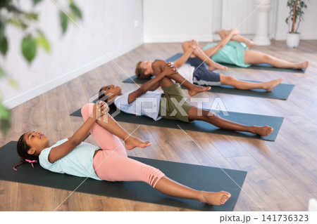 At yoga class African girl is lying on back, bent one leg at knee and raised it to chest At yoga class African girl is lying on back, bent one leg at knee and raised it to chest 141736323