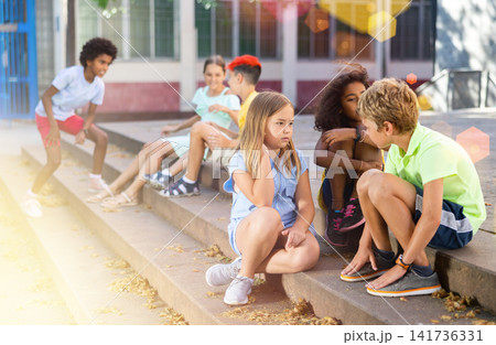 Positive tweenagers friendly blabbing while sitting on steps outdoors Positive tweenagers friendly blabbing while sitting on steps outdoors 141736331