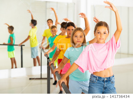 Children standing along ballet bar in dance studio during dance class 141736434