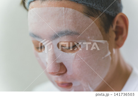 ヘアバンドをつけてシートマスクを顔に密着させる40代男性のフェイスケア ヘアバンドをつけてシートマスクを顔に密着させる40代男性のフェイスケア 141736503