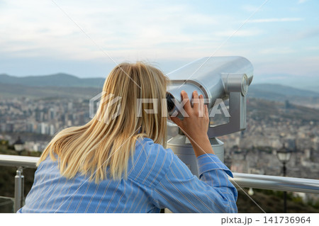 User observes panoramic cityscape with binoculars during golden hour 141736964