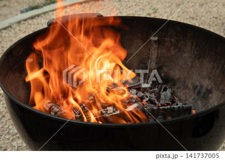 Fire blazes in charcoal grill, illuminating backyard setting. Cooking and socializing concept 141737005