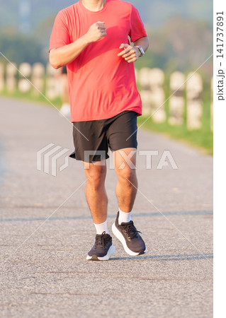 Active young Asian man jogging and running in the public park at morning. Male athlete in sportswear exercising for healthy lifestyle and fitness workout outdoors. Wellness and sport concepts 141737891
