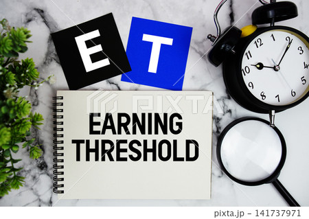 ET Earning Threshold text written on notepad with alarm clock and magnifying glass on marble background ET Earning Threshold text written on notepad with alarm clock and magnifying glass on marble background 141737971