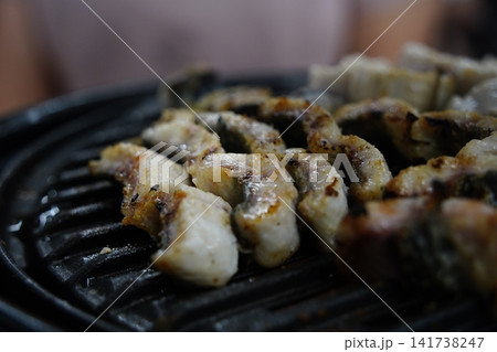 Fresh eels grilling on a charcoal brazier grill close up Fresh eels grilling on a charcoal brazier grill close up 141738247