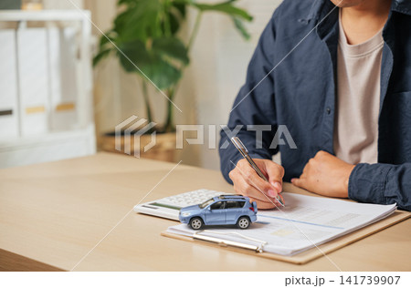 A man writes his signature on a car finance or lease agreement. Great for vehicle buying, renting, or dealership deals emphasizing auto loans 141739907