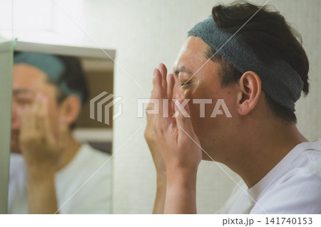 洗面台の鏡の前で化粧水を手のひらで顔全体に馴染ませる40代男性のスキンケア 洗面台の鏡の前で化粧水を手のひらで顔全体に馴染ませる40代男性のスキンケア 141740153