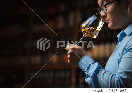 Sommelier Pouring Sample of Wine Into Glass Against Filled Bottles Shelf in Cellar Sommelier Pouring Sample of Wine Into Glass Against Filled Bottles Shelf in Cellar 141740474