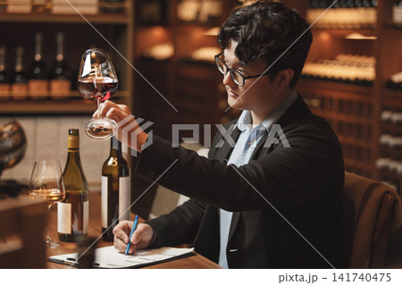 Professional Sommelier Conducts Wine Tasting Session Sitting at Table in Cellar. Professional Sommelier Conducts Wine Tasting Session Sitting at Table in Cellar. 141740475