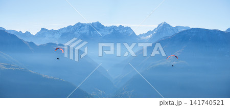 Paragliders flying in sky against mountain range layers on sunny day. Paragliders flying in sky against mountain range layers on sunny day. 141740521