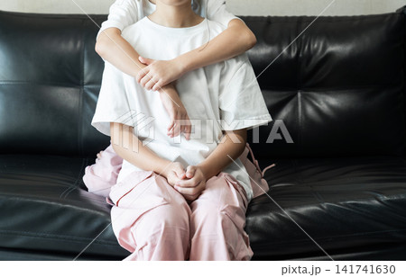 Younger sister hugging her older sister on a black leather sofa, expressing sibling love, affection, family bonding, and childhood togetherness. Younger sister hugging her older sister on a black leather sofa, expressing sibling love, affection, family bonding, and childhood togetherness. 141741630