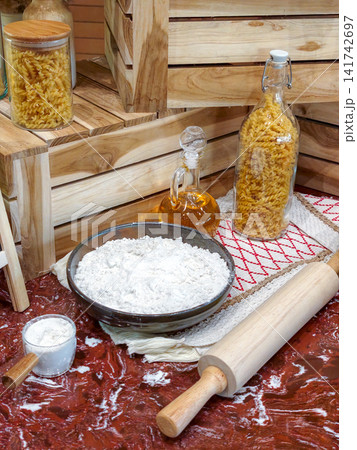 Pasta ingredients with flour, olive oil, and rolling pin on a rustic wooden kitchen table. Pasta ingredients with flour, olive oil, and rolling pin on a rustic wooden kitchen table. 141742697