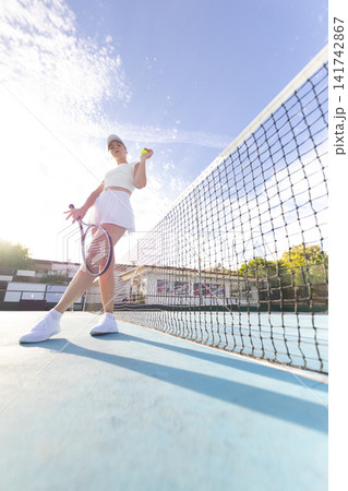 Player practices tennis on a court with clear sky and sunlight in afternoon Player practices tennis on a court with clear sky and sunlight in afternoon 141742867