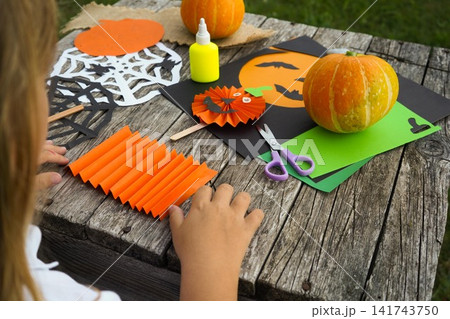 Close up of a little girl sitting at a rustic wooden table outdoors with colorful Halloween craft materials Close up of a little girl sitting at a rustic wooden table outdoors with colorful Halloween craft materials 141743750
