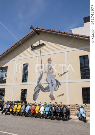 Penang, Malaysia - May 17, 2024: Vespa mural on building with vintage scooters lined up in front, showcasing Italian culture and urban lifestyle in a vibrant city setting Penang, Malaysia - May 17, 2024: Vespa mural on building with vintage scooters lined up in front, showcasing Italian culture and urban lifestyle in a vibrant city setting 141743977