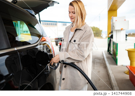 Woman refueling black car at gas station pump Woman refueling black car at gas station pump 141744908
