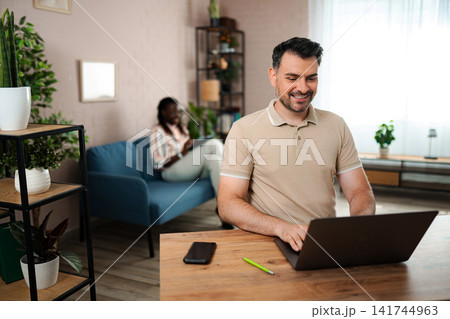 Man using laptop working from home with partner 141744963