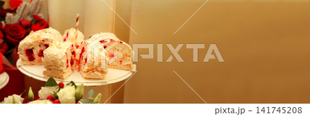 Gourmet dessert table concept featuring sliced meringue roulade cake with berry filling and almond flakes next to floral arrangements, festive celebration and confectionery background Gourmet dessert table concept featuring sliced meringue roulade cake with berry filling and almond flakes next to floral arrangements, festive celebration and confectionery background 141745208