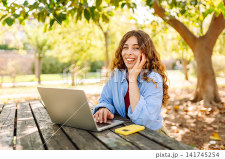 Attractive woman working or studying at laptop as sitting in city park. Freelancer working in park. 141745254