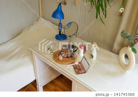 Modern makeup table with cosmetics and mirror on wooden desk. Eyeshadow palettes, beauty blenders, makeup brushes, perfume bottle on table. Concept of self care. Beauty Routine, Everyday Makeup Setup Modern makeup table with cosmetics and mirror on wooden desk. Eyeshadow palettes, beauty blenders, makeup brushes, perfume bottle on table. Concept of self care. Beauty Routine, Everyday Makeup Setup 141745360