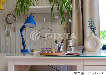 Modern makeup table with cosmetics and mirror on wooden desk. Eyeshadow palettes, beauty blenders, makeup brushes, perfume bottle on table. Concept of self care. Beauty Routine, Everyday Makeup Setup Modern makeup table with cosmetics and mirror on wooden desk. Eyeshadow palettes, beauty blenders, makeup brushes, perfume bottle on table. Concept of self care. Beauty Routine, Everyday Makeup Setup 141745361