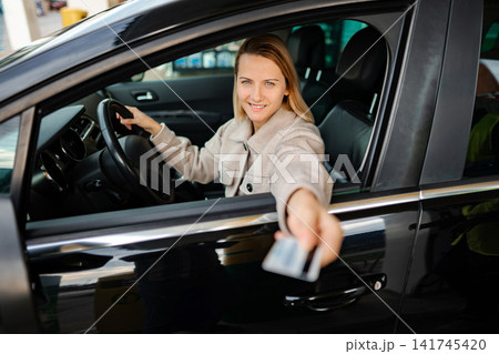 Woman paying with credit card while driving car Woman paying with credit card while driving car 141745420