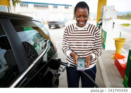 Woman paying for gasoline using mobile phone at gas station 141745430