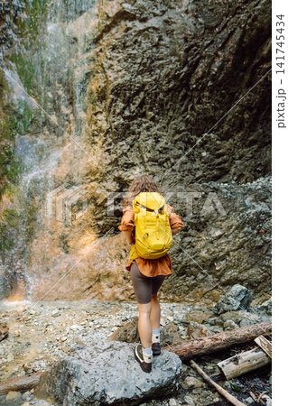 Smiling female dressed in hiking clothes, enjoys a waterfall near a mountain river. Travel, trekking Smiling female dressed in hiking clothes, enjoys a waterfall near a mountain river. Travel, trekking 141745434