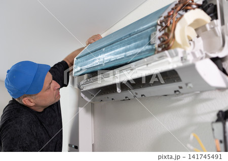 Technician repairing air conditioner. Man fixing indoor cooling unit. Maintenance service, air conditioning. 141745491
