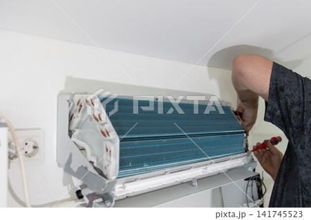 Technician repairing air conditioner on wall. Professional worker fixing cooling system. HVAC maintenance. Technician repairing air conditioner on wall. Professional worker fixing cooling system. HVAC maintenance. 141745523