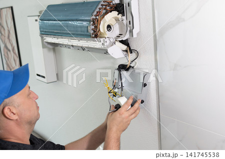 Technician repairing wall mounted air conditioner unit. Professional maintenance service in bright room. 141745538