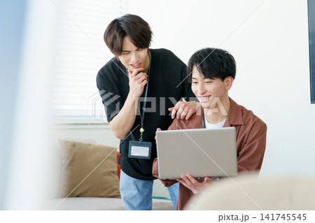オフィスでノートパソコンを見ながら会話する若い日本人男性2人 141745545
